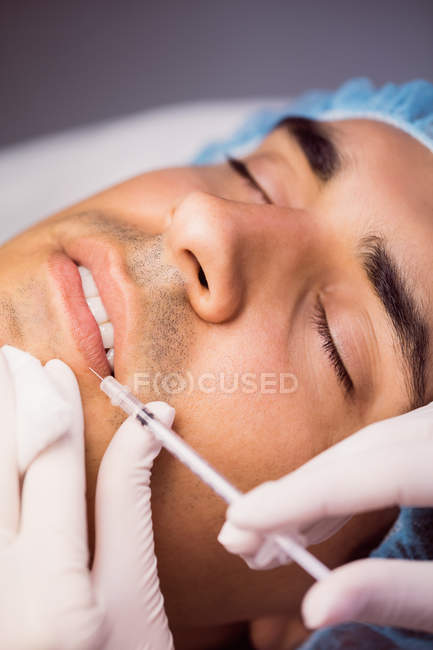 Hombre que recibe inyección de botox en los labios en la clínica - foto de stock