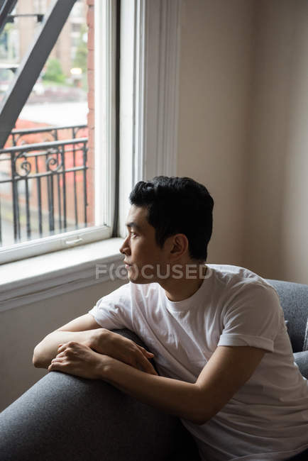 Задумчивый человек смотрит в окно на дом — стоковое фото