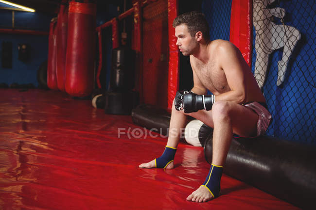 Thoughtful boxer sitting on punching bag in fitness studio — Stock Photo