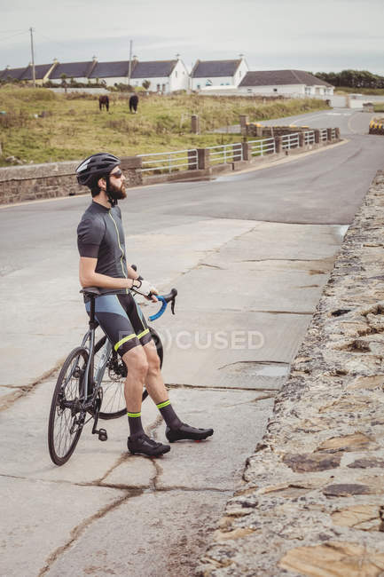 Athlete standing with bicycle on country road — Stock Photo