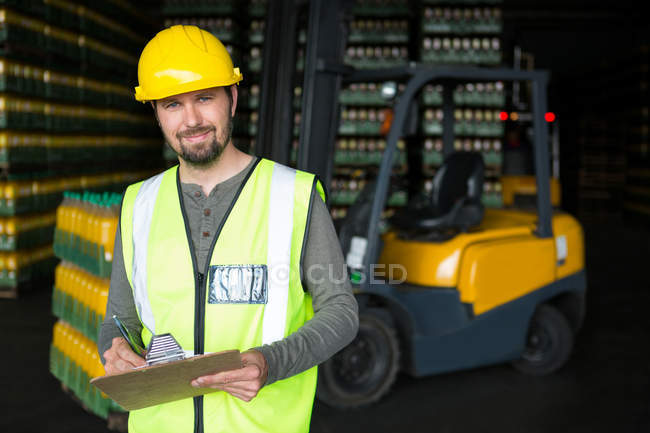 Retrato de sorridente trabalhador do sexo masculino escrevendo na área de transferência no armazém — Fotografia de Stock