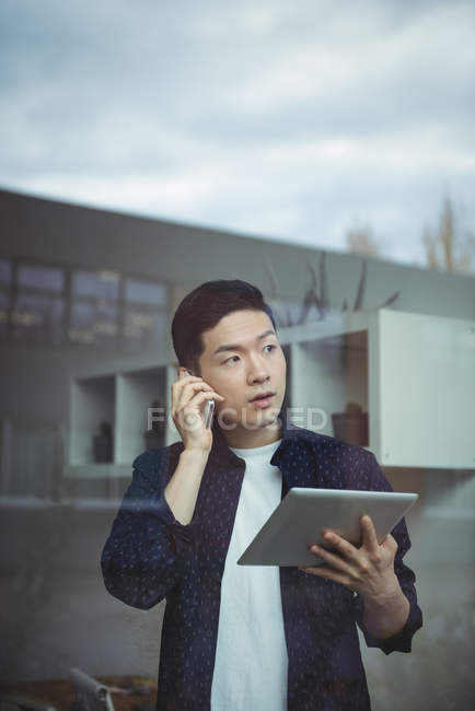 Ejecutivo de negocios hablando en el teléfono móvil mientras usa la tableta digital en la oficina - foto de stock
