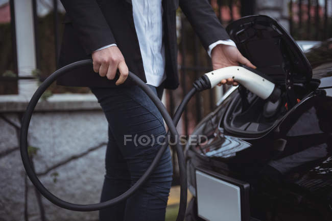 Partie médiane de la femme rechargeant la voiture électrique à la station de recharge du véhicule — Photo de stock