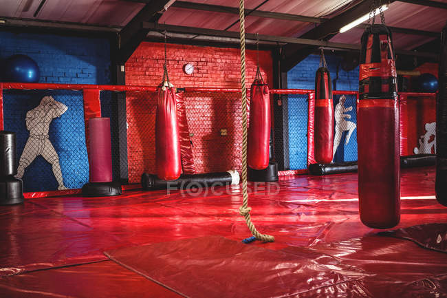 Red punching bags and rope hanging on fitness studio — Stock Photo