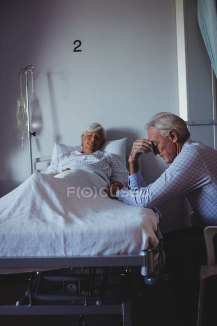 Ill woman sleeping on bed while worried man sitting beside her bed in the hospital — Stock Photo