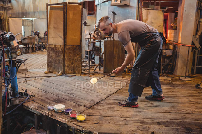 Glassblower attaching colored glass to a piece of hot molten glass at glassblowing factory — Stock Photo