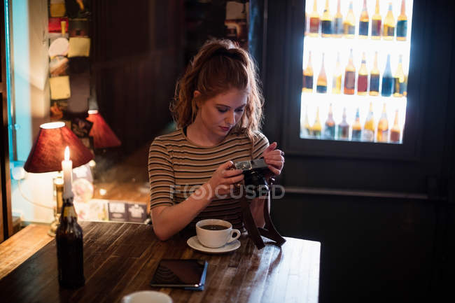 Belle femme vérifiant les photos dans l'appareil photo numérique au bar — Photo de stock
