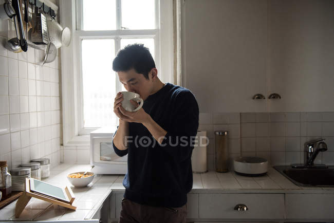 Homem usando tablet digital enquanto toma uma xícara de café em casa — Fotografia de Stock