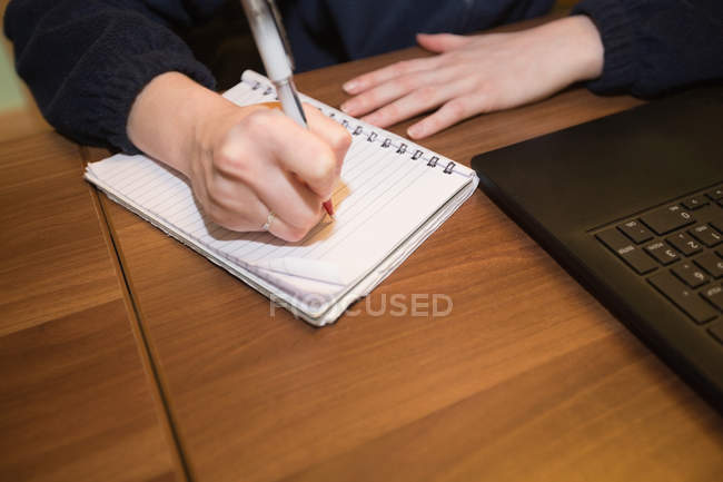 Nahaufnahme einer Frau, die im Büro am Schreibtisch sitzt und auf einem Notizbuch schreibt — Stockfoto