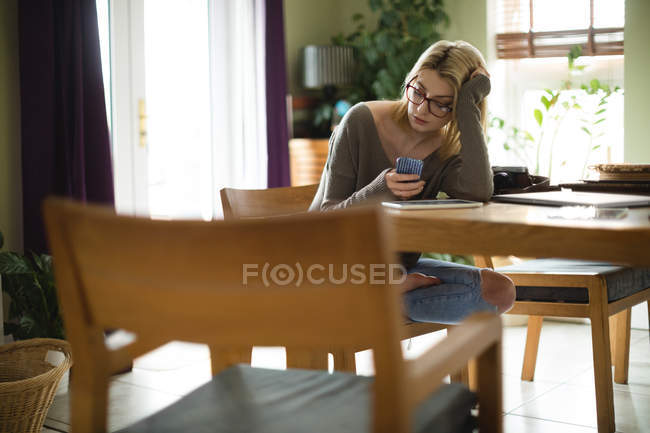 Mujer usando el teléfono móvil mientras está sentado en casa - foto de stock