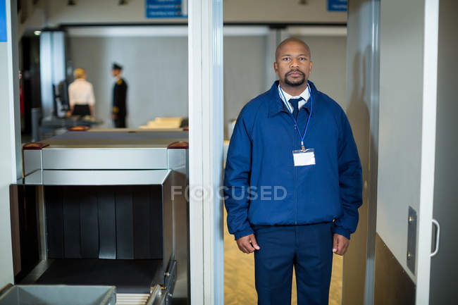 Retrato del oficial de seguridad del aeropuerto parado en la puerta del detector de metales en la terminal del aeropuerto - foto de stock