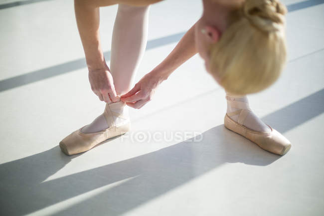 Ballerina tying her ballet shoes in the studio — Stock Photo