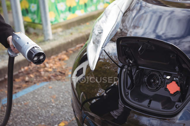 Hand of man holding car charger at electric vehicle charging station — Stock Photo