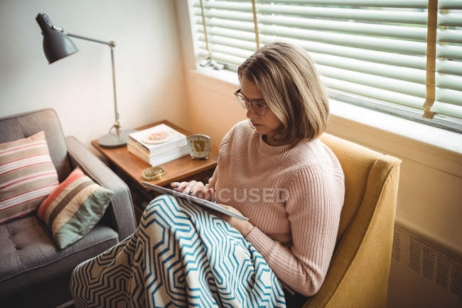 Woman sitting on chair using digital tablet in living room at home — Stock Photo
