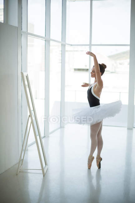 Ballerina practicing ballet dance in front of mirror in studio fit, mid woman - Stock Photo #225311314