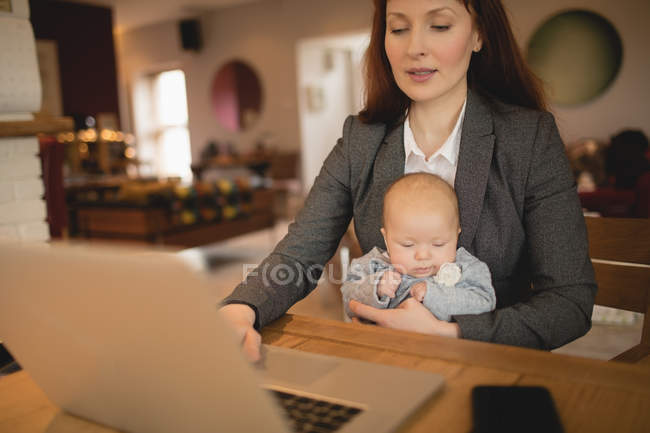 Мати використовує ноутбук, тримаючи новонароджену дитину вдома — стокове фото