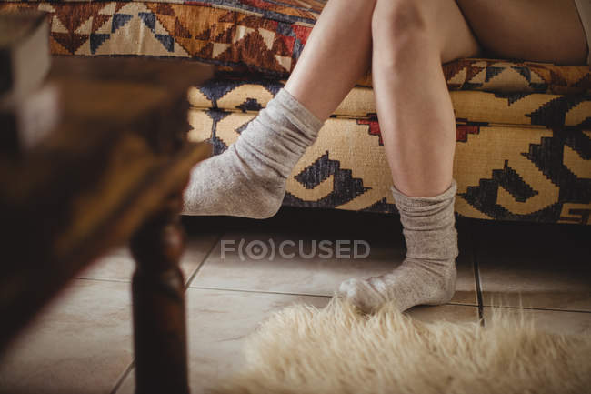 Frau in Socken sitzt zu Hause auf Sofa mit gekreuzten Beinen — Stockfoto
