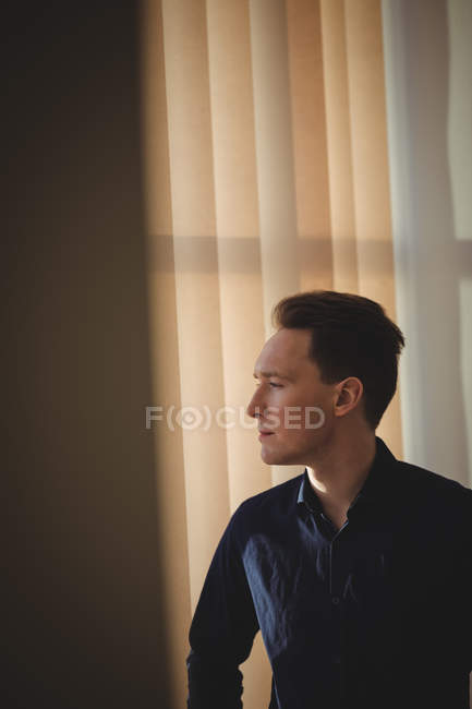 Male executive standing near window blinds in office — Stock Photo