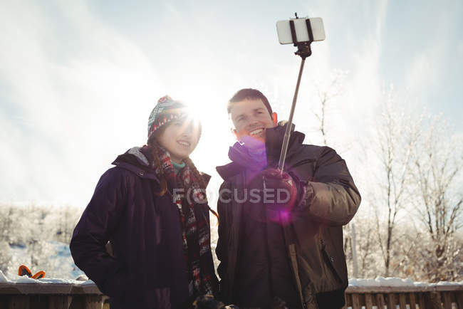 Happy skier  couple clicking a selfie with selfie stick in ski resort — Stock Photo