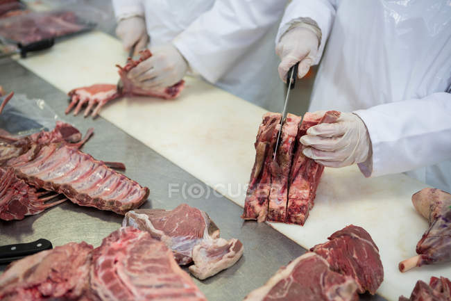 Primer plano de los carniceros que cortan carne en la fábrica de carne - foto de stock