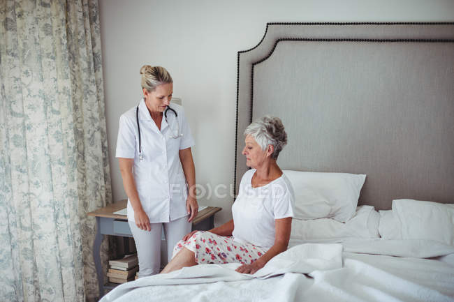 Doctora interactuando con paciente mayor en casa - foto de stock