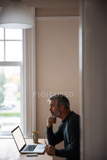 Задумчивый мужчина сидит с ноутбуком в гостиной дома — стоковое фото