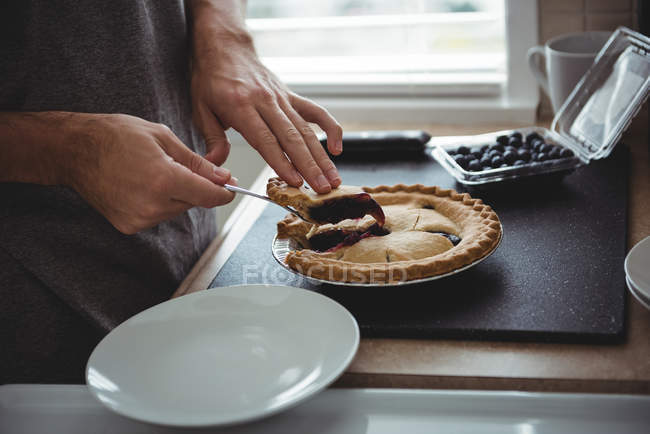 Mid-section of man removing slice of blueberry tart in kitchen — Stock Photo