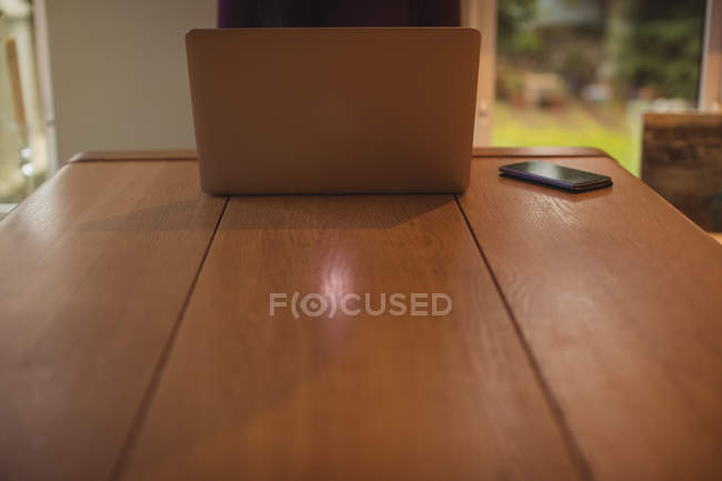 Computer portatile e telefono cellulare su tavolo in legno a casa — Foto stock