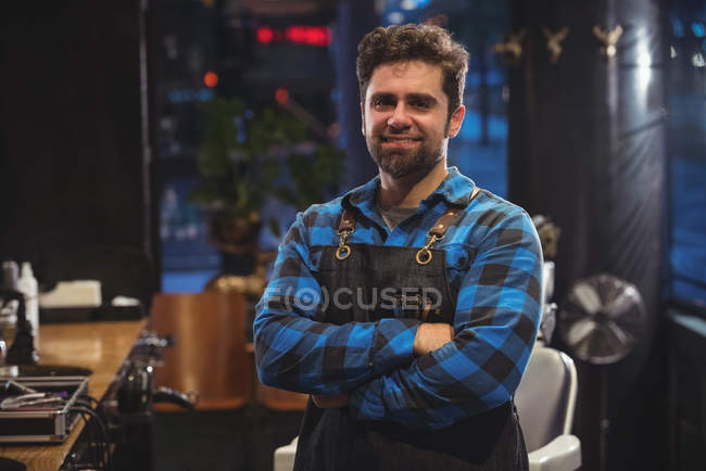 Front view of male barber standing with arms crossed in barber shop — Stock Photo
