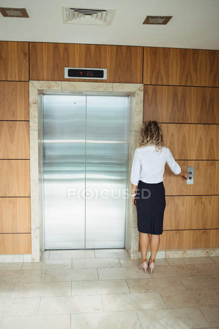 Rückansicht einer Geschäftsfrau, die auf einen Aufzug im Büro wartet — Stockfoto