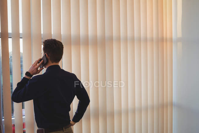 Вид ззаду чоловічий виконавчий виступ на мобільному телефоні біля віконних жалюзі — стокове фото