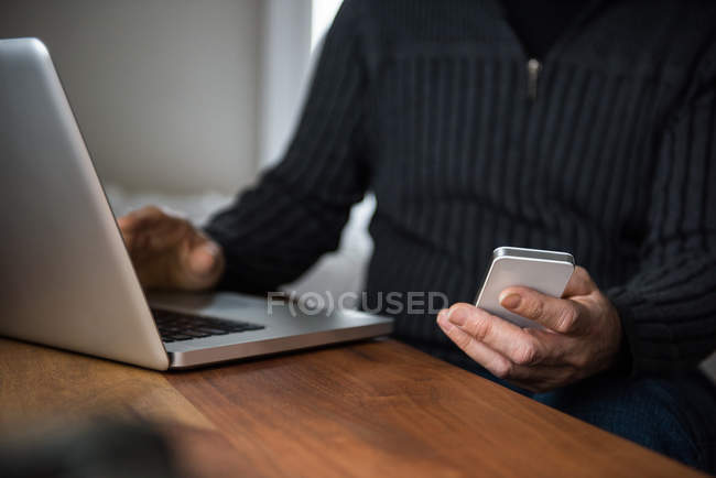 Mid-section of man using laptop and mobile phone at home — Stock Photo