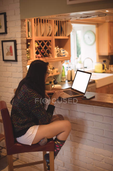 Жінка сидить і використовує ноутбук на кухонній стійці вдома — стокове фото