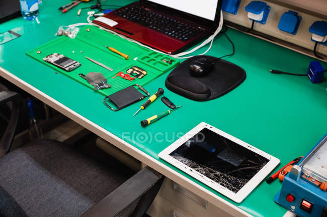 Tableta digital dañada y teléfono móvil en un centro de reparación - foto de stock