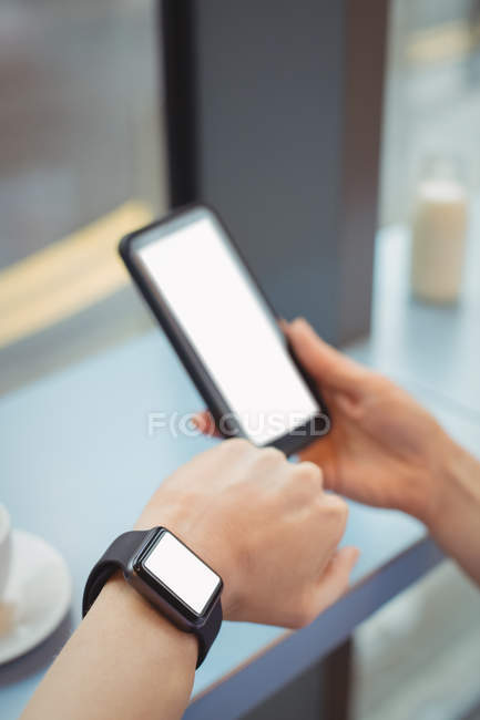Hands of businesswoman using mobile and checking time at counter in cafeteria — Stock Photo