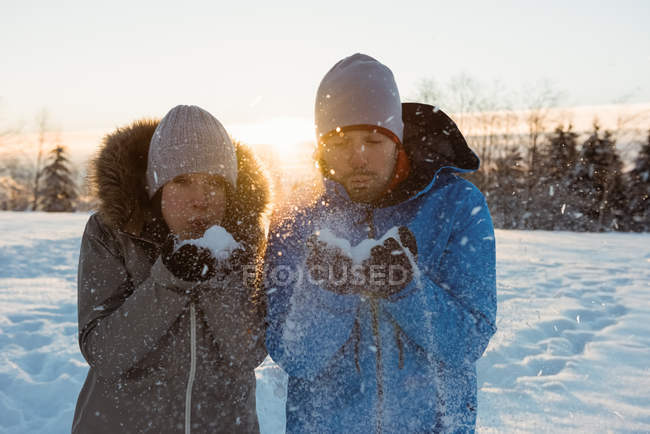 Casal soprando neve e desfrutando no dia ensolarado de inverno — Fotografia de Stock
