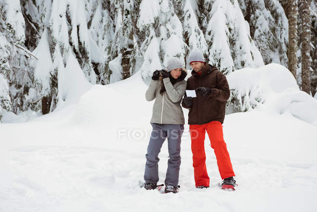 Couple with address card looking through binoculars on snowy landscape — Stock Photo