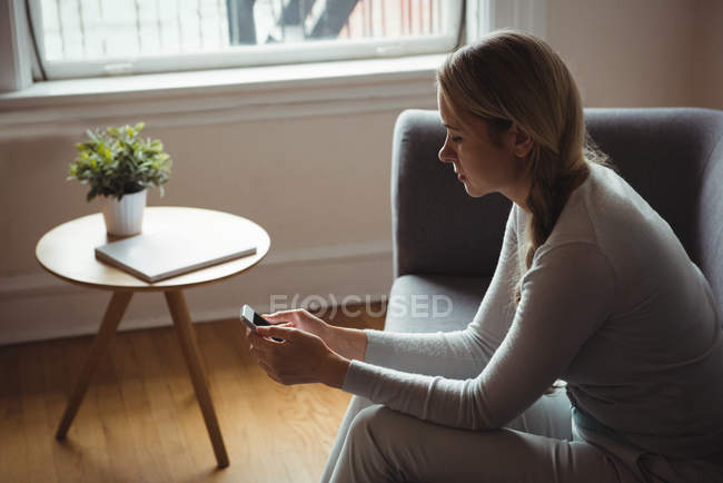 Mujer usando teléfono móvil en la sala de estar en casa - foto de stock