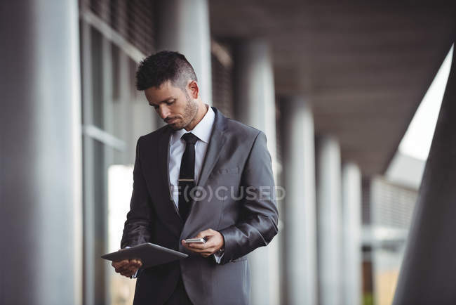 Businessman using digital tablet and mobile phone in office campus — Stock Photo
