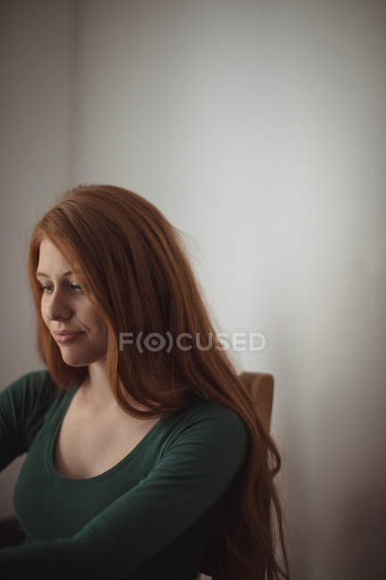 Руда жінка сидить в приміщенні і, дивлячись — стокове фото