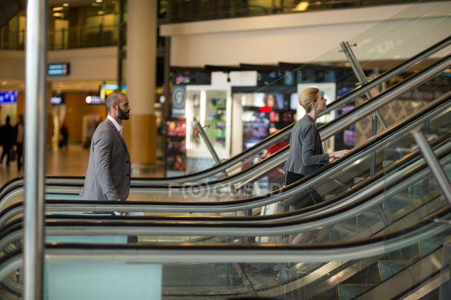 Gente de negocios con equipaje de pie en escaleras mecánicas en la terminal del aeropuerto - foto de stock