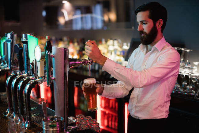 Бармен наливает пиво из барного насоса на стойке бара — стоковое фото