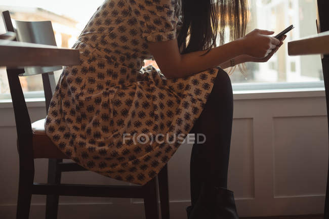 Femme utilisant un téléphone portable près de la fenêtre au café — Photo de stock