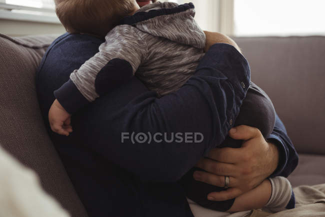 Partie médiane du père tenant son bébé assis sur le canapé à la maison — Photo de stock