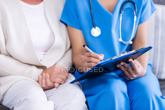 Midsection of doctor writing on clipboard in clinic — Stock Photo