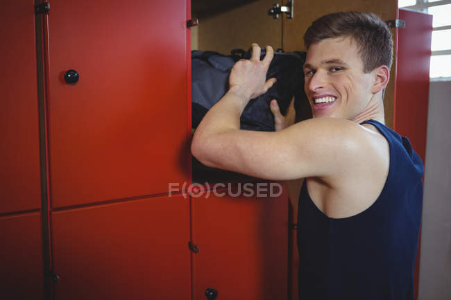 Sportsman sorrindo mantendo saco no armário no vestiário — Fotografia de Stock