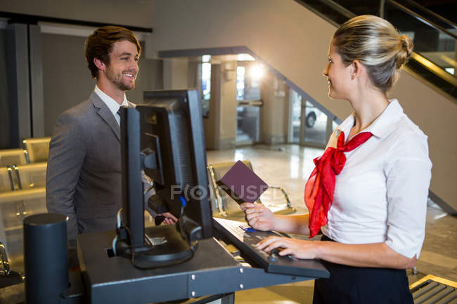 Бизнесмен, взаимодействующий с сотрудницами аэропорта за стойкой регистрации в терминале аэропорта — стоковое фото