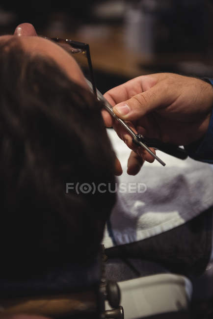 Close-up de homem recebendo barba raspada com navalha na barbearia — Fotografia de Stock