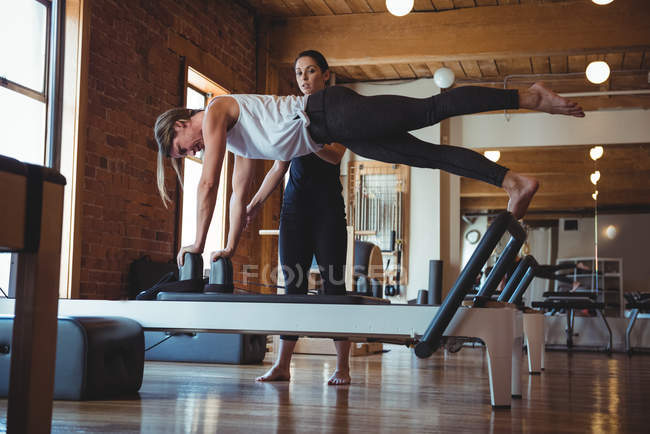 Instructeur aidant une femme tout en pratiquant le pilates dans un studio de fitness — Photo de stock