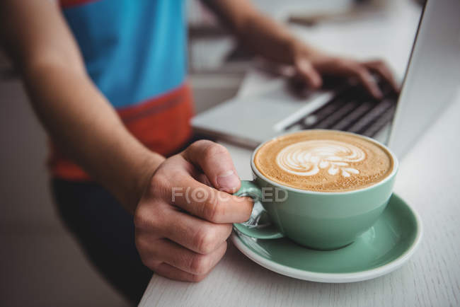 Seção média do homem usando laptop e segurando uma xícara de café no café — Fotografia de Stock